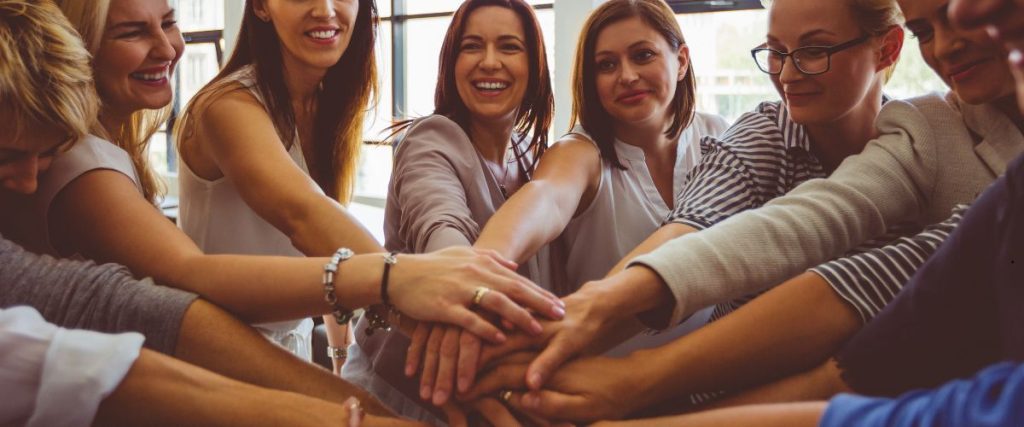 Grupo de mujeres sonriendo y con las manos entrelazadas haciendo un circulo